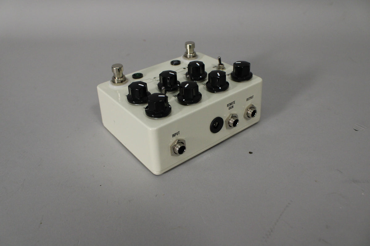 Angled view of the off-white pedal, showing its top with eight black knobs and two footswitches, plus the side with three jacks.
