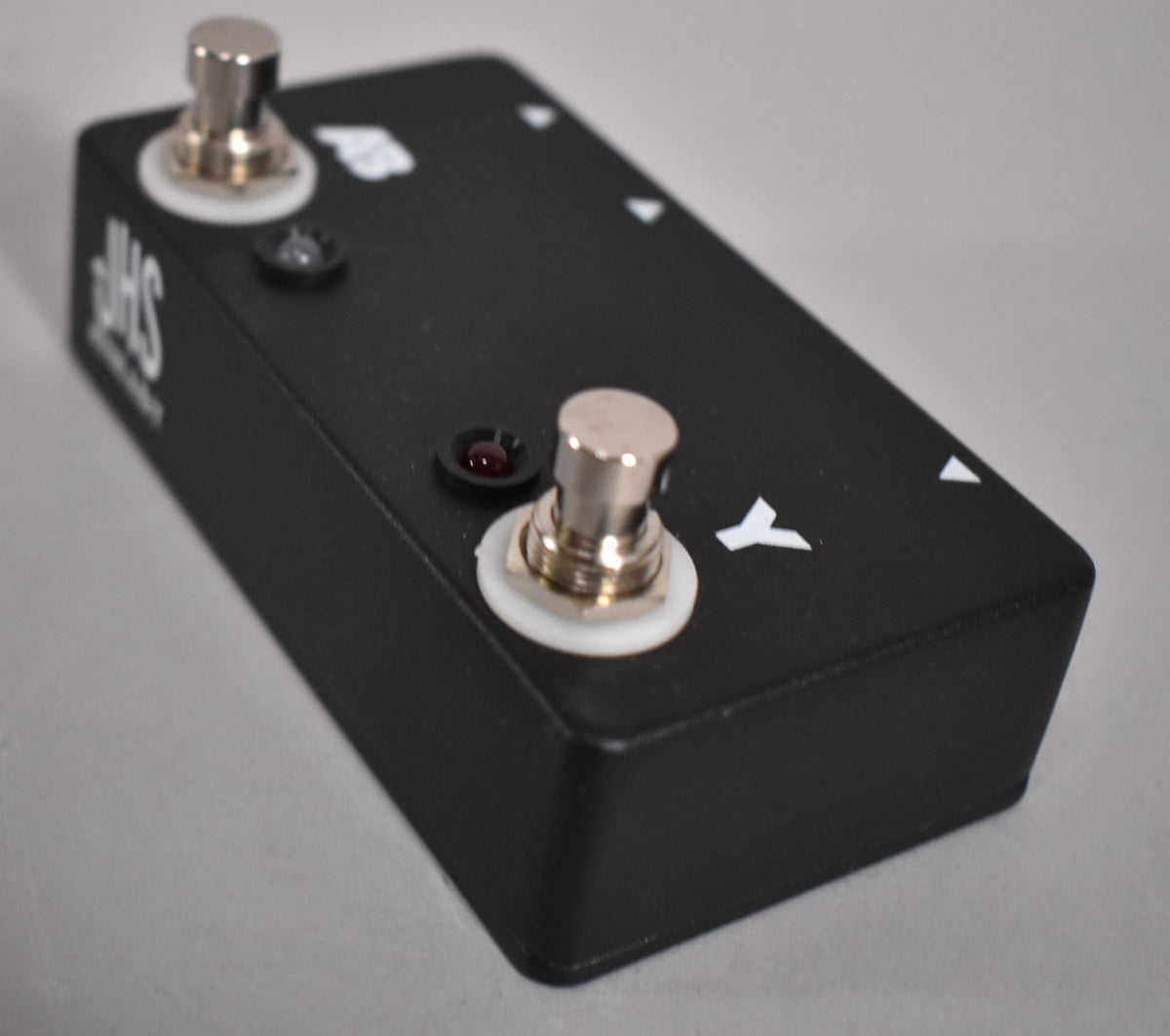 A black rectangular pedal with two chrome footswitches, two red indicator lights, and white lettering, viewed from the top right.