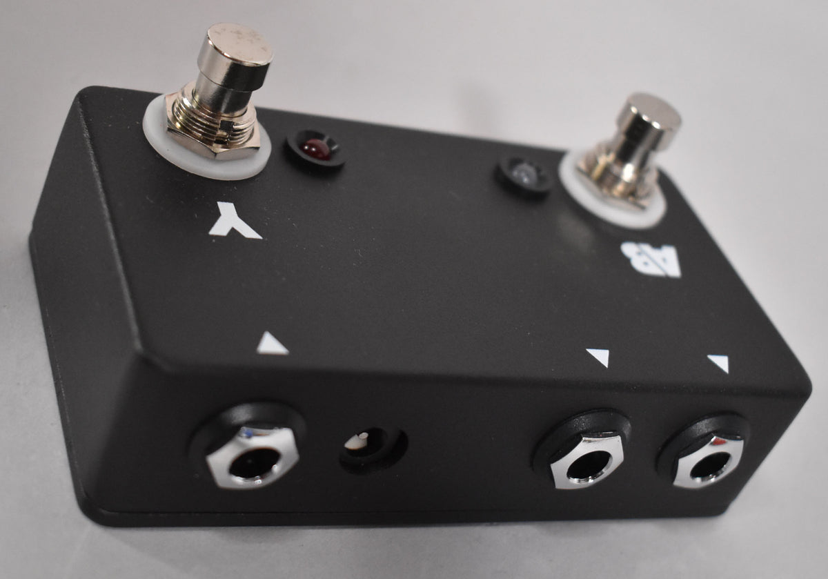 A black guitar pedal with two chrome footswitches, two red indicator lights, and three chrome input jacks along the front edge.