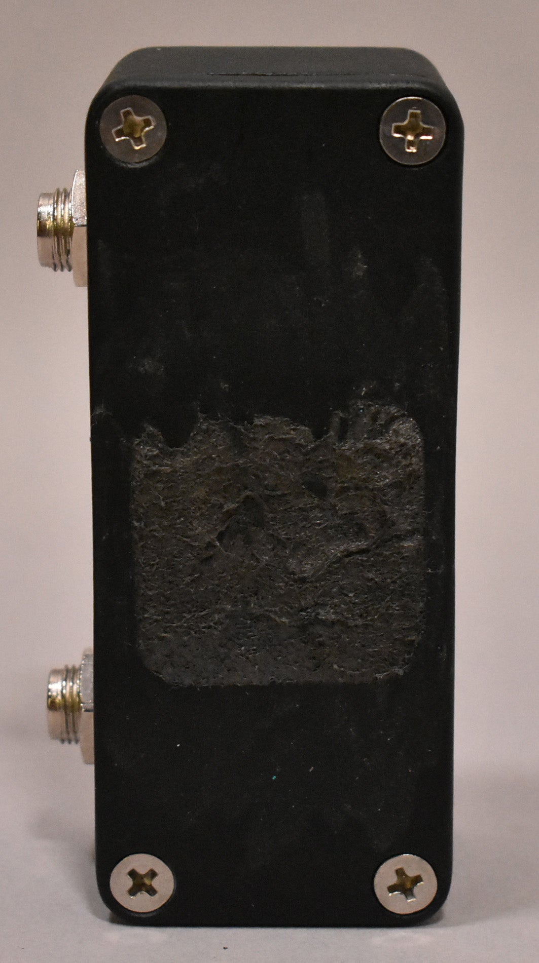 The black pedal's right side is shown, with two silver jacks and four silver screws, and a large patch of worn texture.