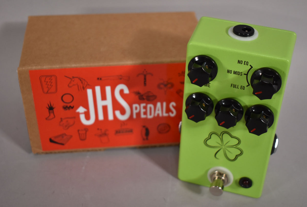 A bright green pedal with a four-leaf clover graphic, five black knobs, and a footswitch, next to its brown cardboard box.