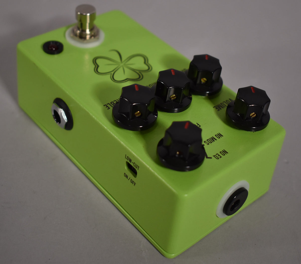 Bright green pedal with a four-leaf clover graphic, five black knobs with red indicators, a footswitch, and a small toggle switch.