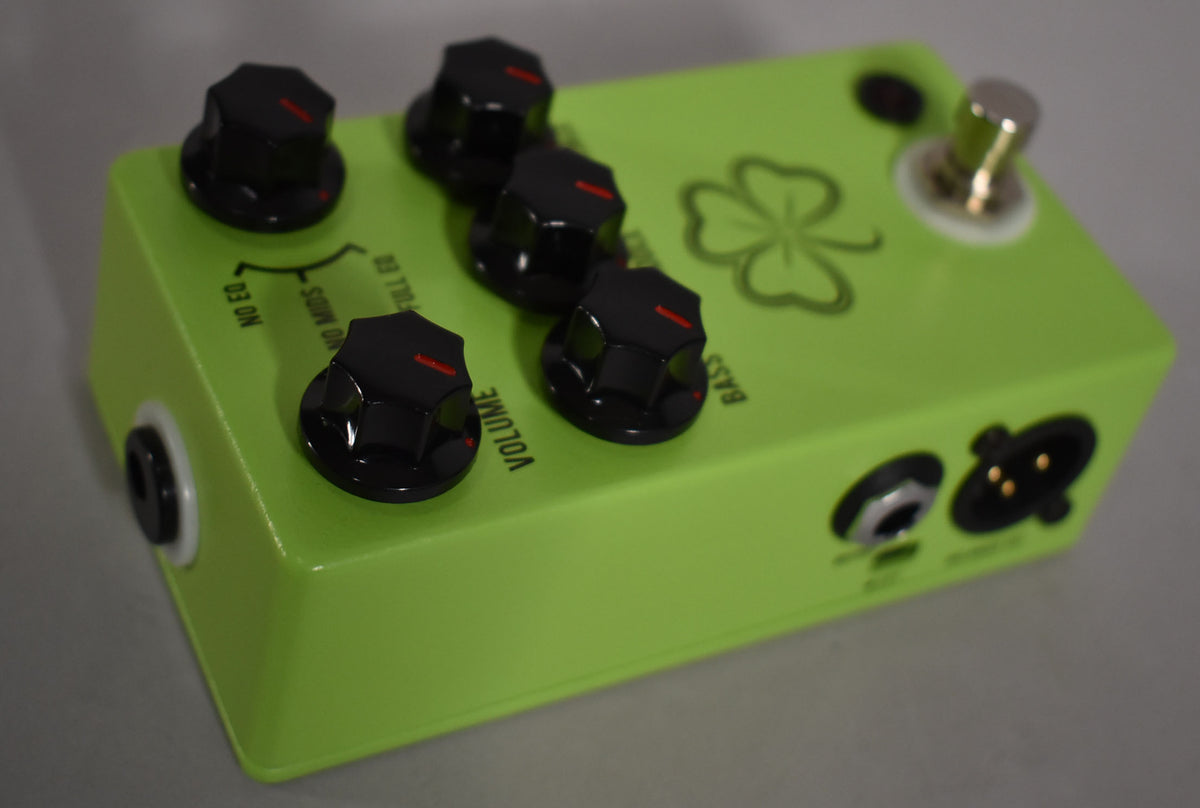 A bright green pedal with a four-leaf clover graphic, five black control knobs with red indicators, a footswitch, and two input jacks.