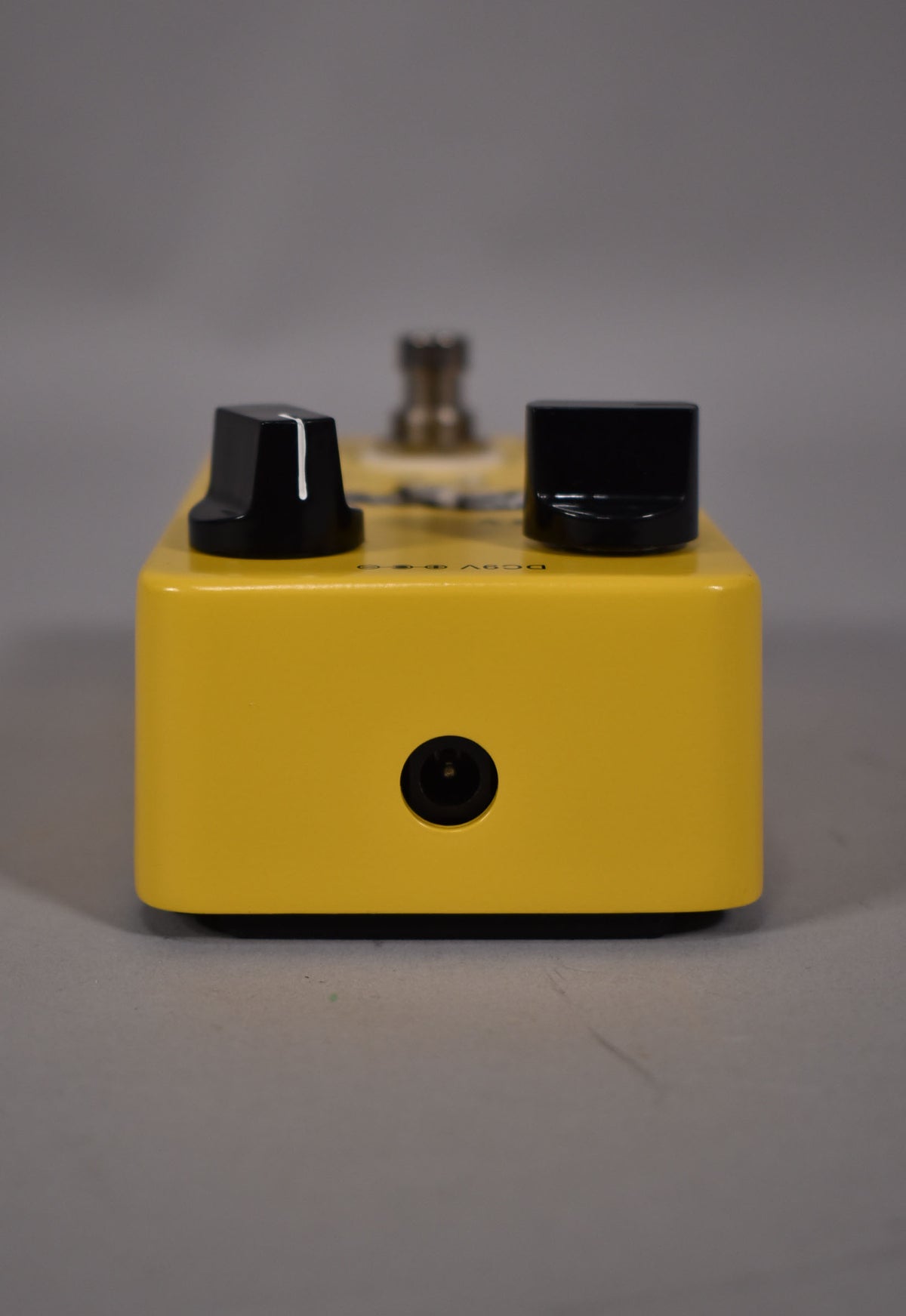 The bright yellow pedal is viewed from the front, showing a DC power input jack and two black control knobs on top.