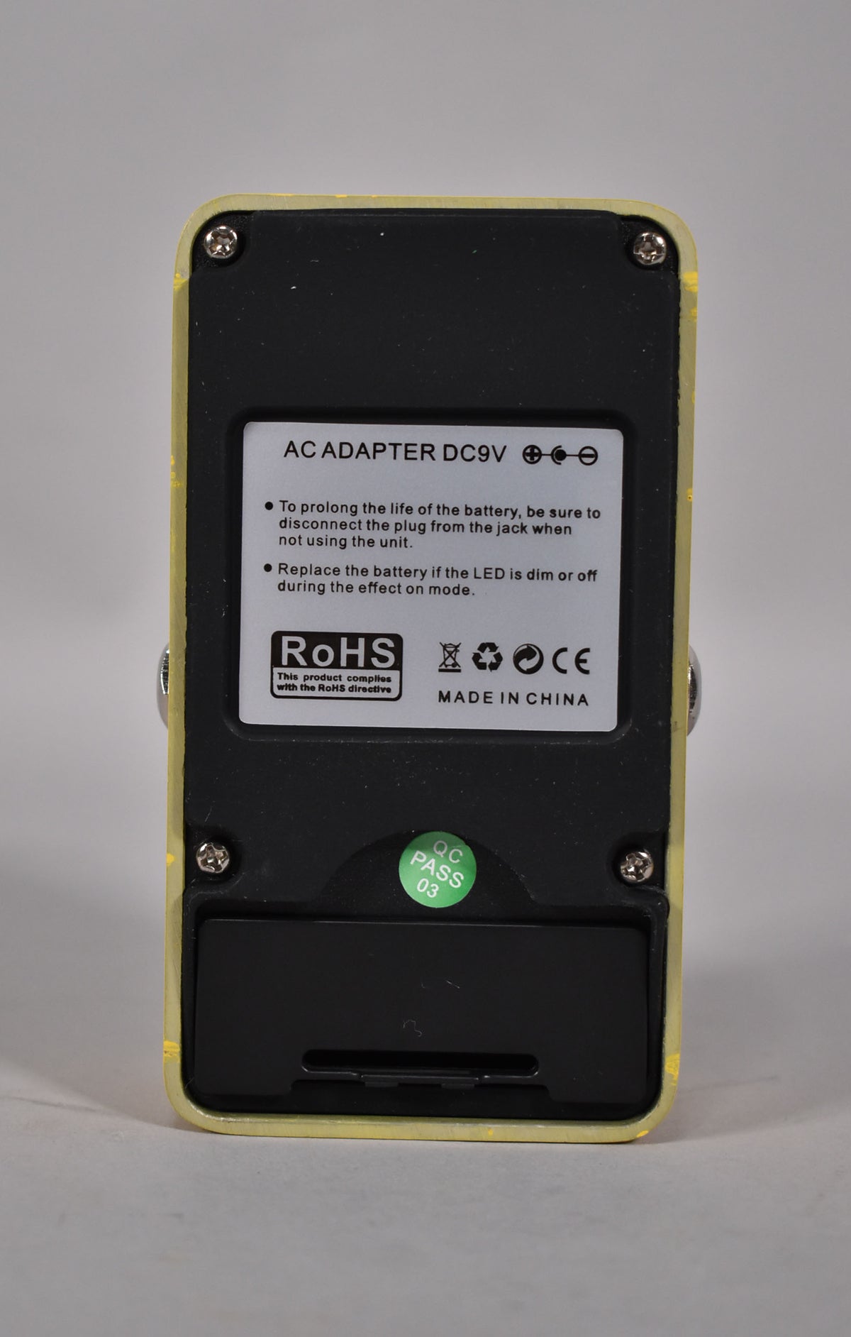 The pedal's yellow casing is seen from the back, revealing a black battery compartment and a white label with text.