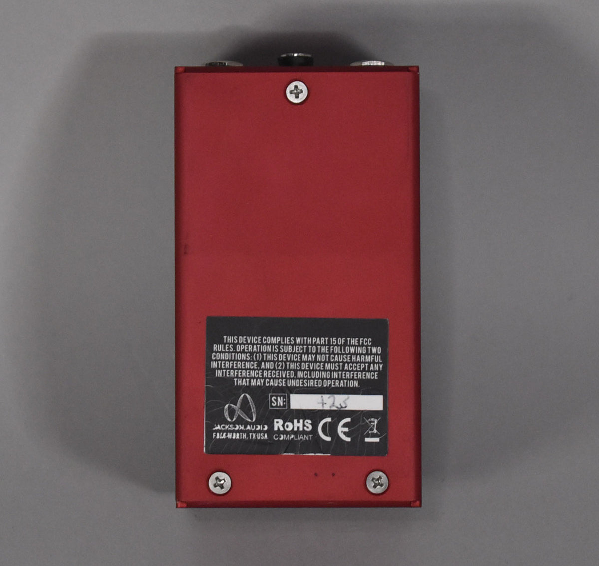 The red rectangular pedal is viewed from the back, showing a black label with white text and four silver screws.
