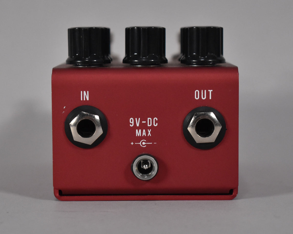 The red pedal's rear panel shows "IN" and "OUT" jacks, a 9V-DC power input, and three black control knobs on top.