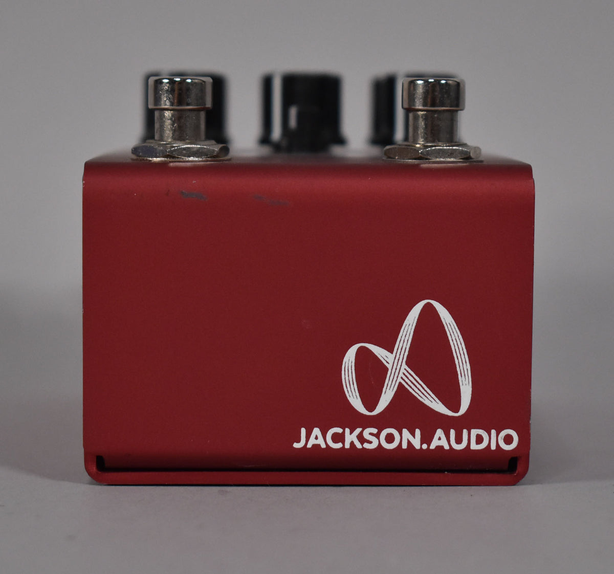 The red pedal is viewed from the front, showing a white logo and two silver footswitches with minor scuffs.