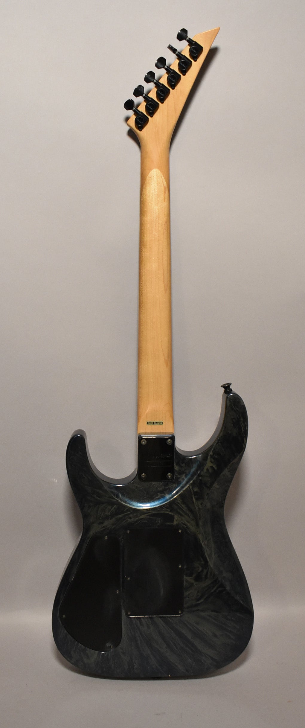 The back of a blue swirl electric guitar, showing the light wood neck, black headstock tuners, and two black control cavity covers.