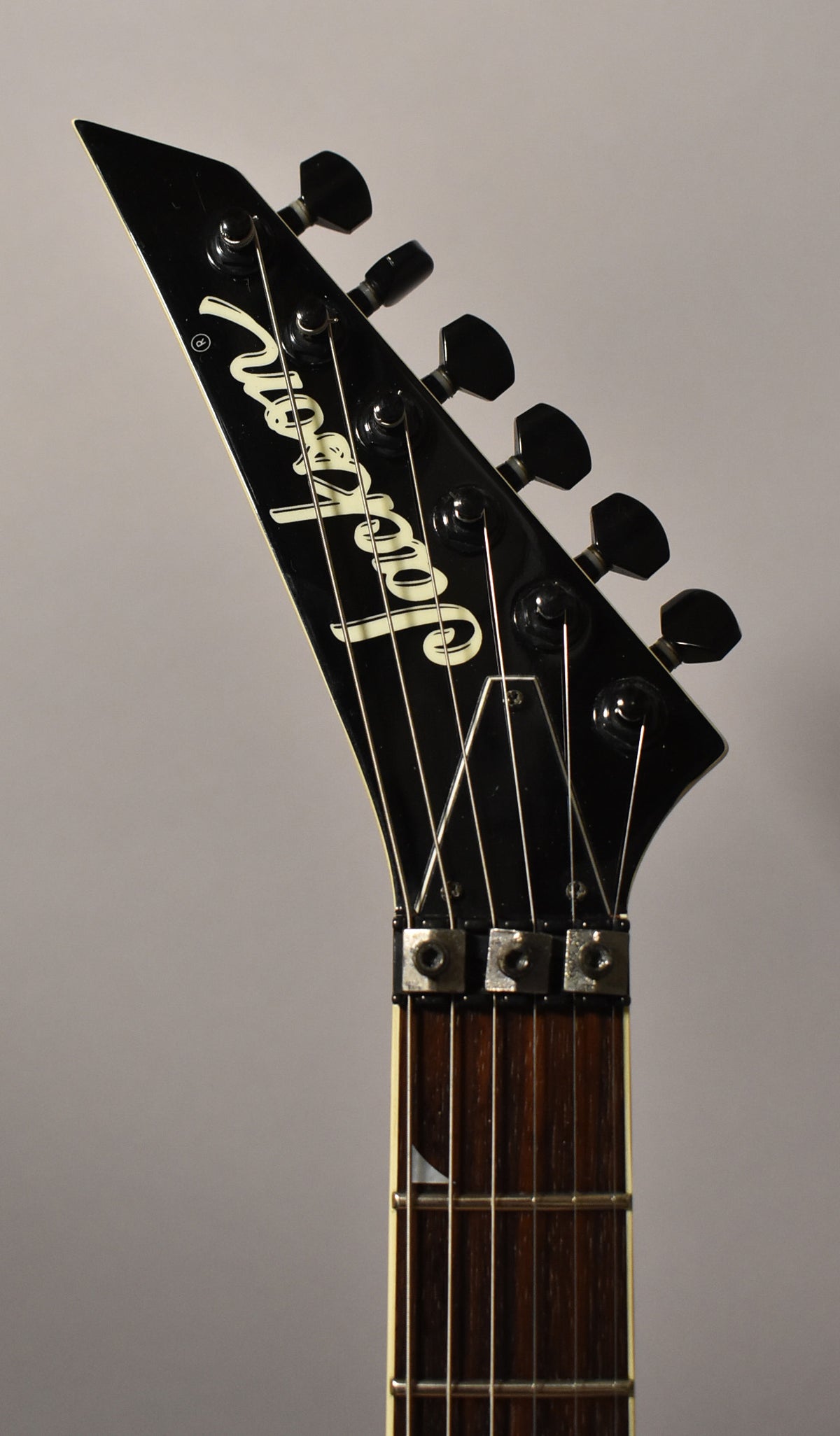 Close-up of the black pointed headstock with six black tuners, a locking nut, and a dark rosewood fretboard.