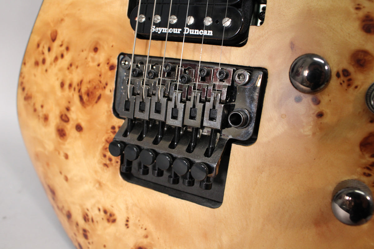 Close-up of the guitar's body, showing the light wood grain with dark figuring, black Floyd Rose bridge, and two dark chrome knobs.