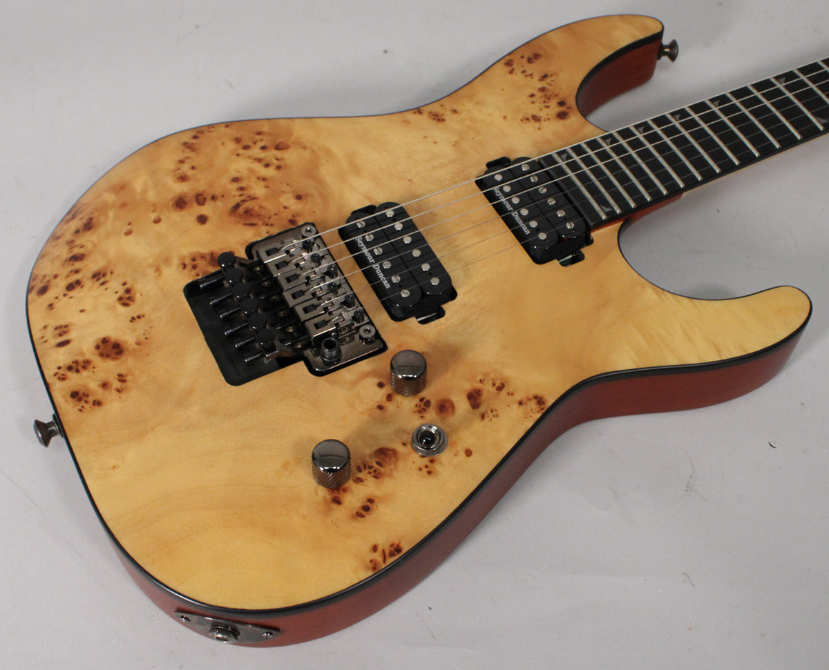 Light-colored electric guitar with a burl wood top, black humbucker pickups, a Floyd Rose bridge, and three chrome knobs.