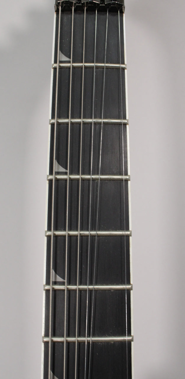 Close-up of the guitar's dark fretboard with six strings, showing white sharkfin inlays on the bass side and a white binding.