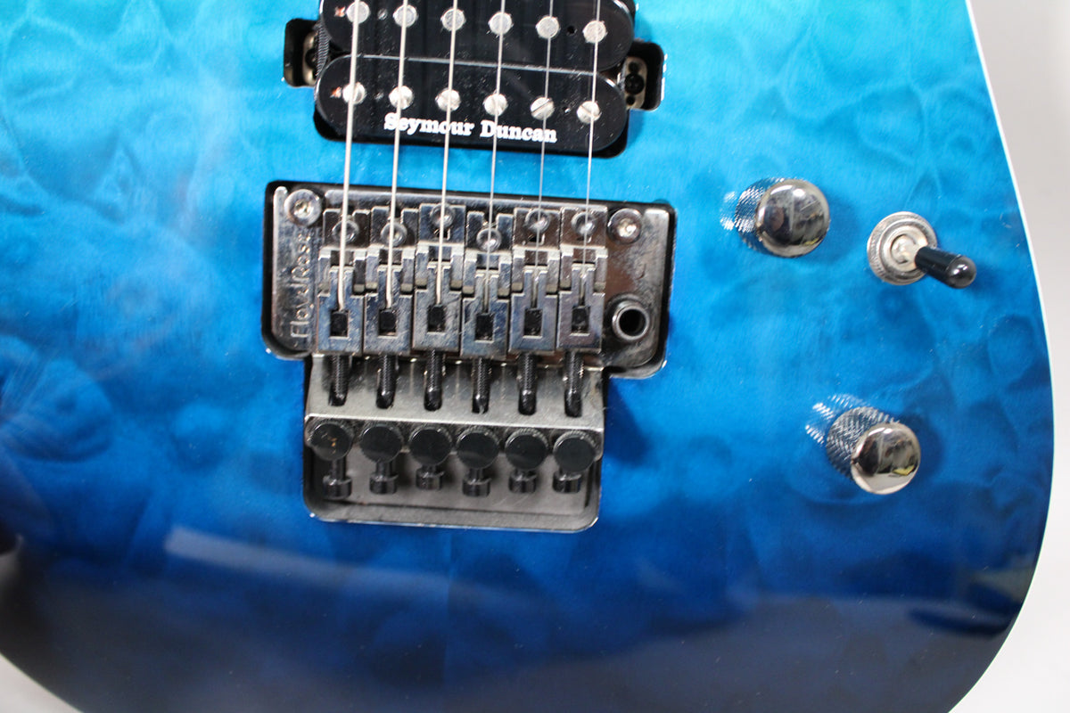 Close-up of the guitar's quilted blue finish, showing the Floyd Rose tremolo system, a Seymour Duncan humbucker, and chrome controls.