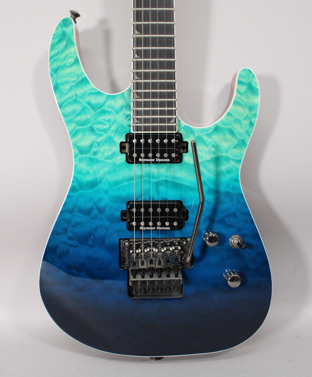The electric guitar's body, from neck to bottom, fades from teal to dark blue with a quilted maple finish, featuring two humbuckers and a tremolo arm.