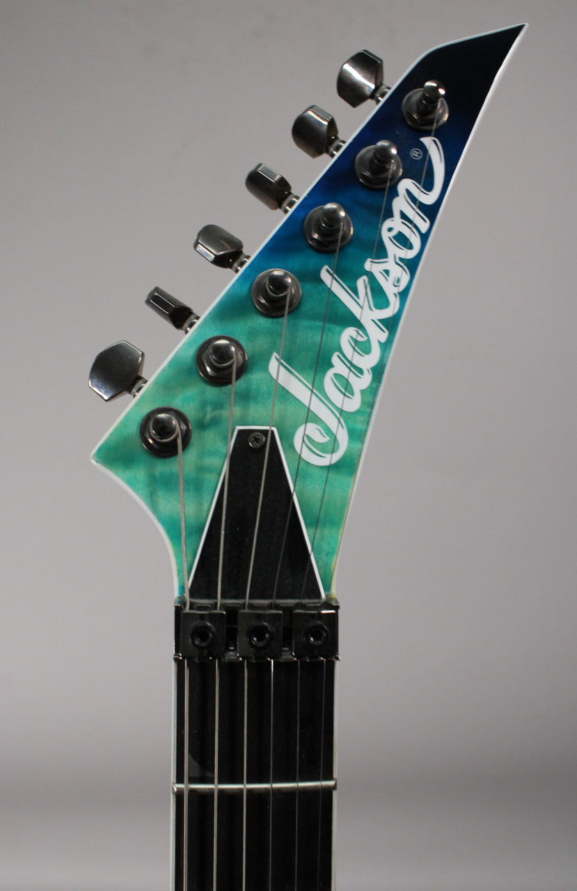 The headstock of a Jackson electric guitar, featuring a quilted maple Caribbean blue fade finish and black tuning pegs.
