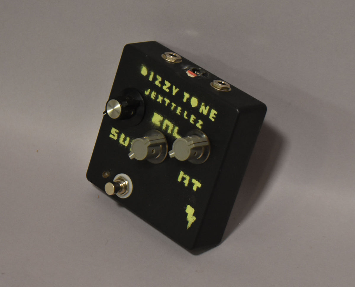 Black fuzz pedal, angled from the right, showing three silver knobs, one black knob, a footswitch, and three input jacks.