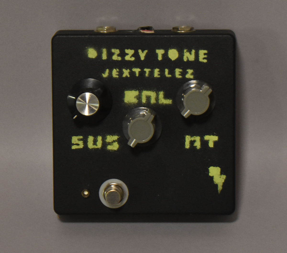 Black fuzz pedal with three gray knobs, one black knob, a footswitch, and distressed yellow lettering.
