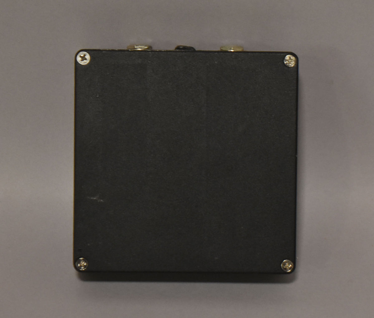 Top-down view of the black fuzz pedal, showing its textured finish, four silver screws, and two gold-colored jacks along the top edge.