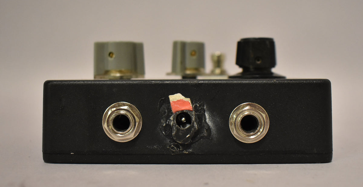 The black fuzz pedal's rear panel shows two input jacks flanking a worn power input with a torn red sticker.