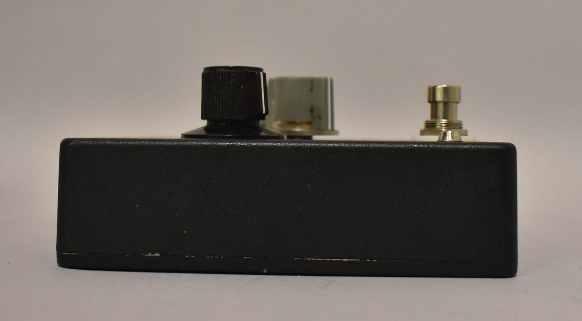 Side view of the black fuzz pedal, showing a black knob, a lighter grey knob, and a silver footswitch, with minor wear along the bottom edge.