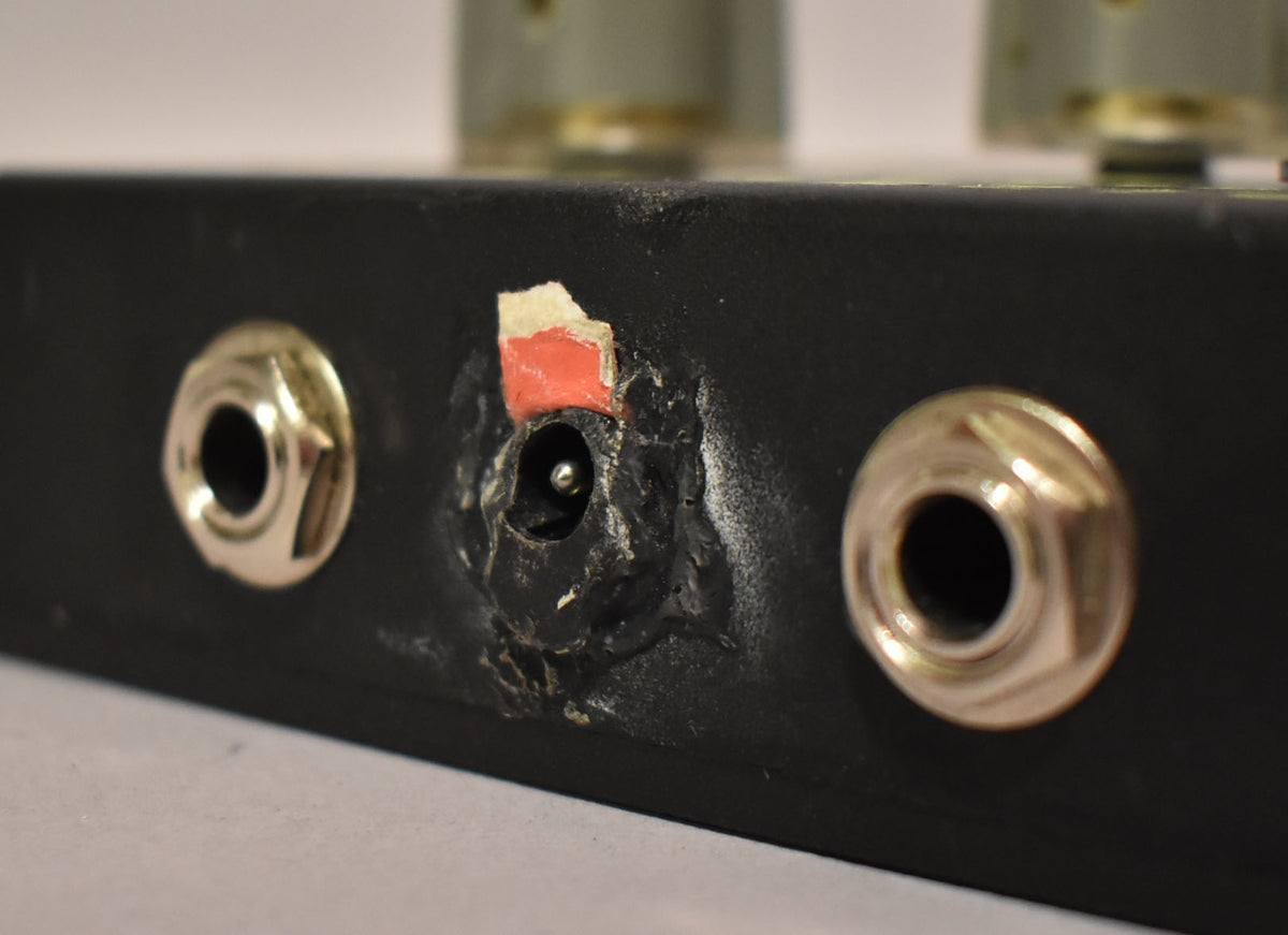 Close-up of the pedal's black side, showing two silver input jacks flanking a worn power input with exposed wiring and a torn red label.