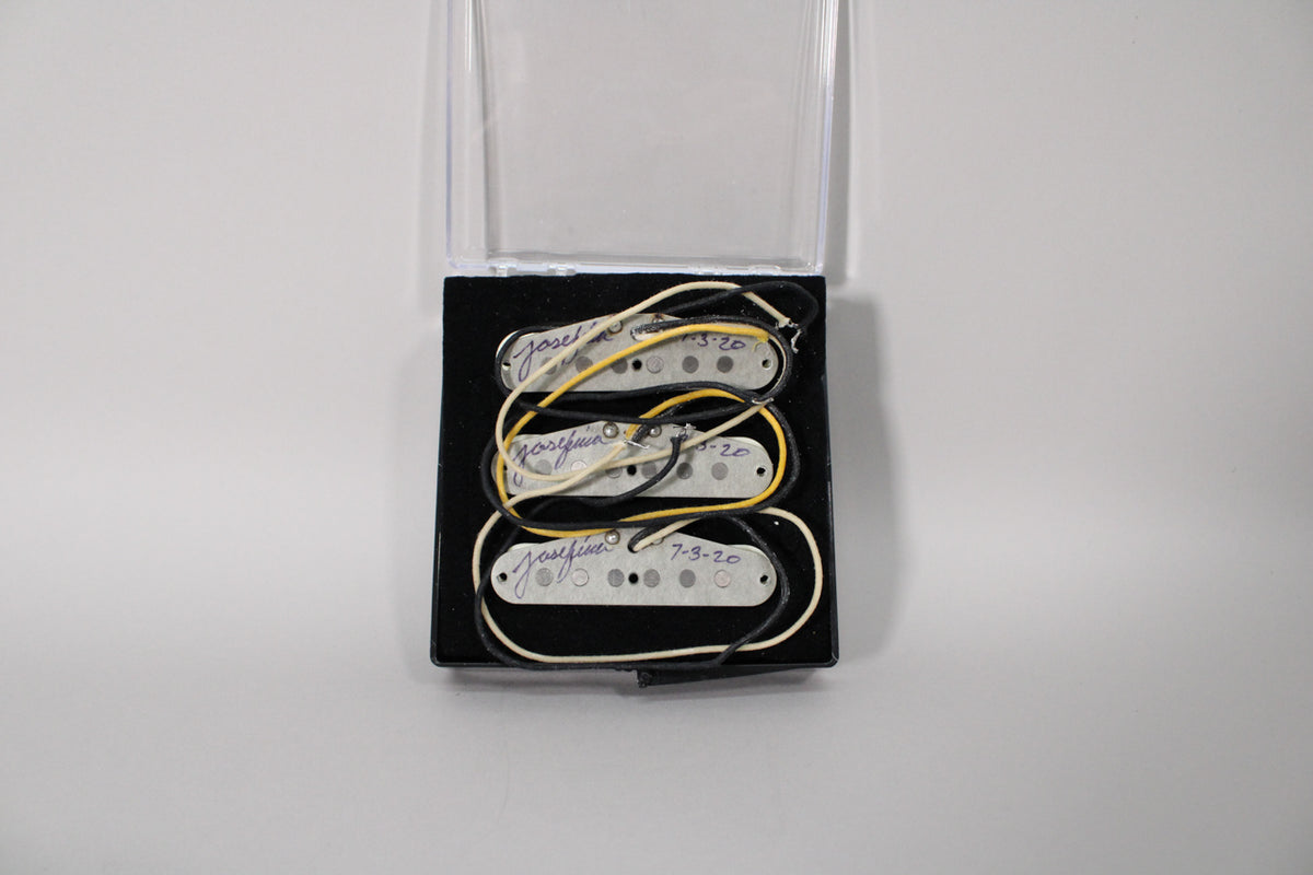 Three white Stratocaster pickups with visible pole pieces and black, yellow, and white wiring, in a black velvet case.