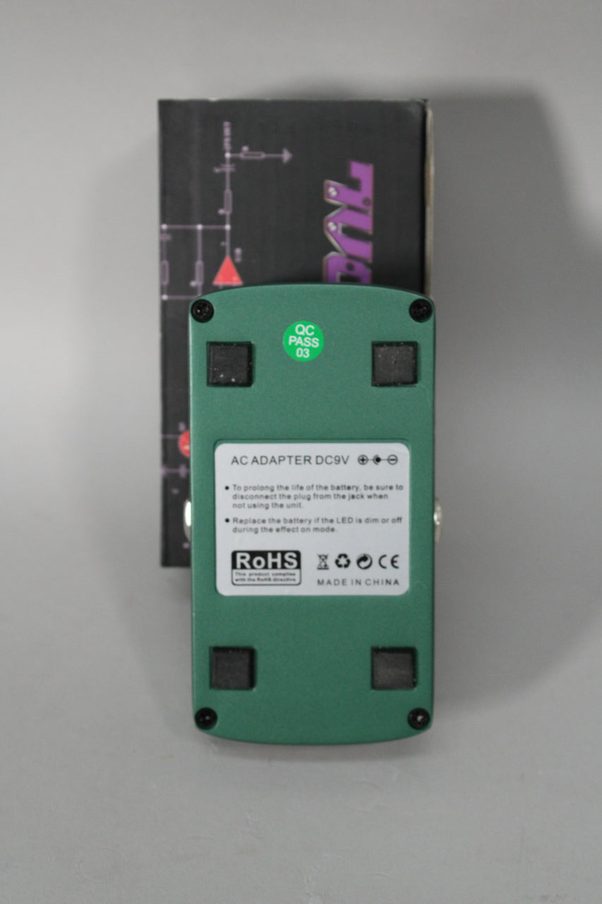 The green pedal's underside is visible, showing a white label with power info, a "QC PASS" sticker, and four black rubber feet.
