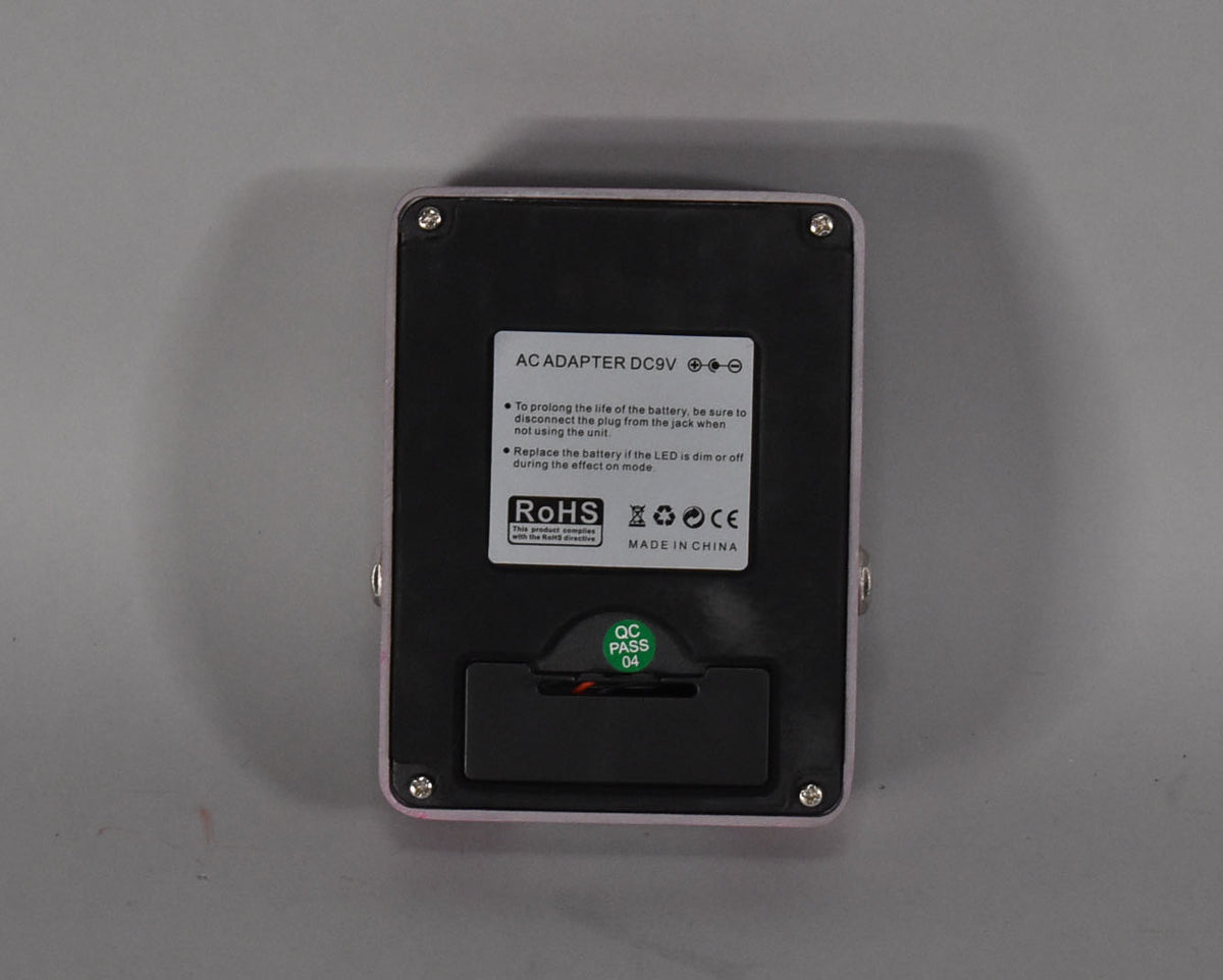 The fuchsia pedal's underside is shown, featuring a black battery compartment cover and a "QC PASS 04" sticker.
