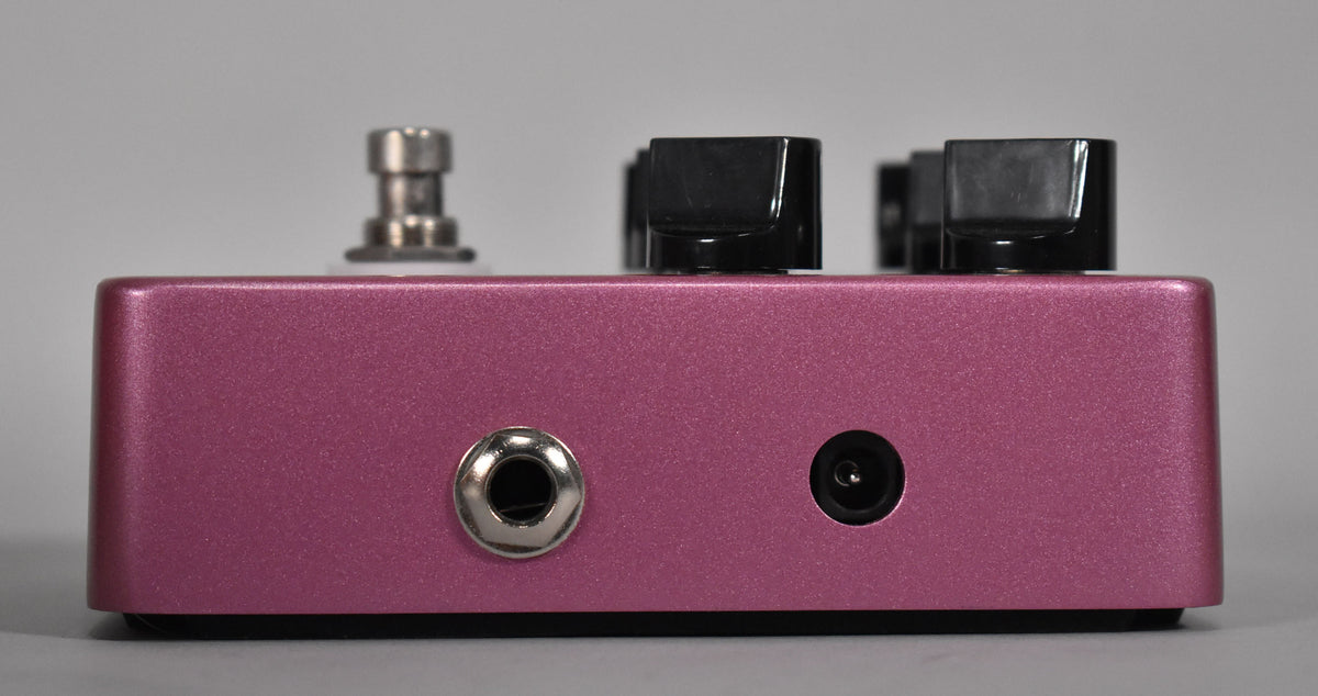 The fuchsia pedal is viewed from the side, showing a silver input jack and a black power input on the right.