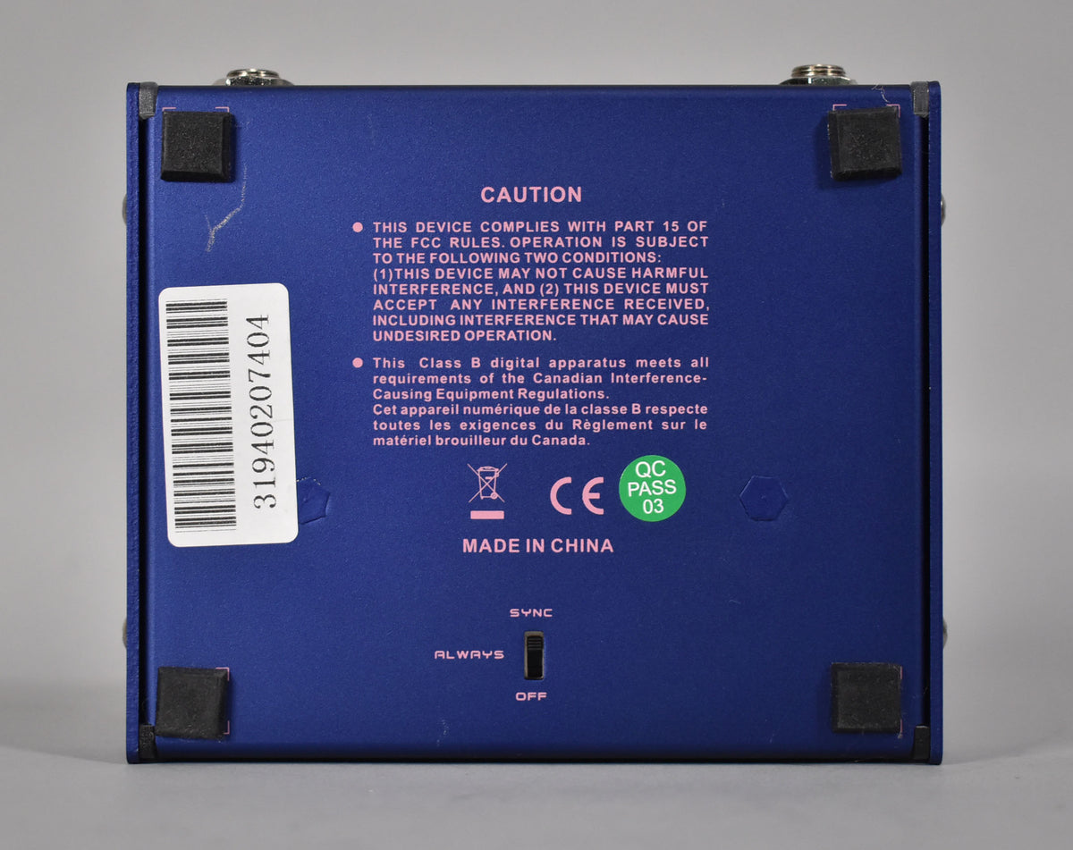 The purple pedal's underside is visible, showing four black rubber feet, a barcode sticker, and a small "SYNC" toggle switch.