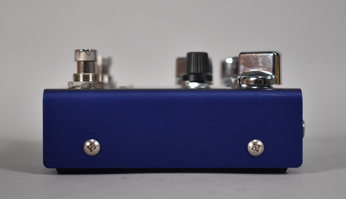 The purple pedal is viewed from the side, showing two silver screws on the front face and three knobs on top.
