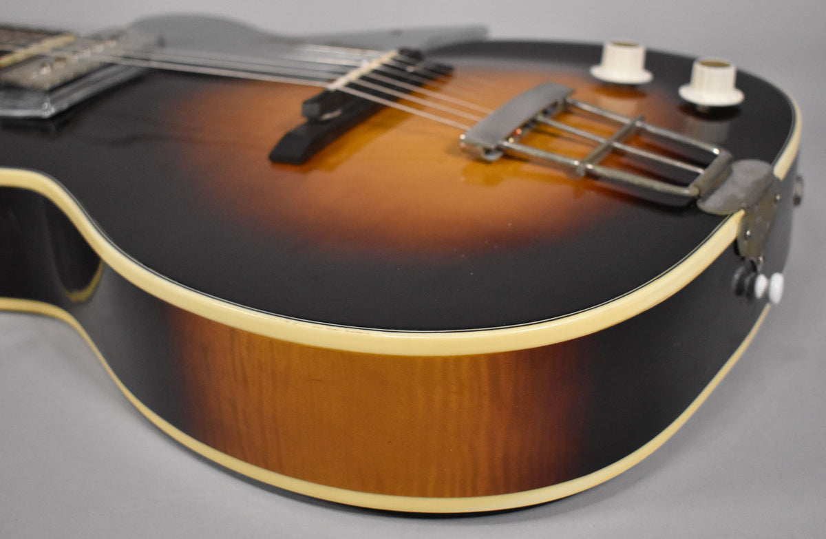 Close-up of the sunburst archtop guitar body, showing the chrome trapeze tailpiece, two cream control knobs, and cream binding.
