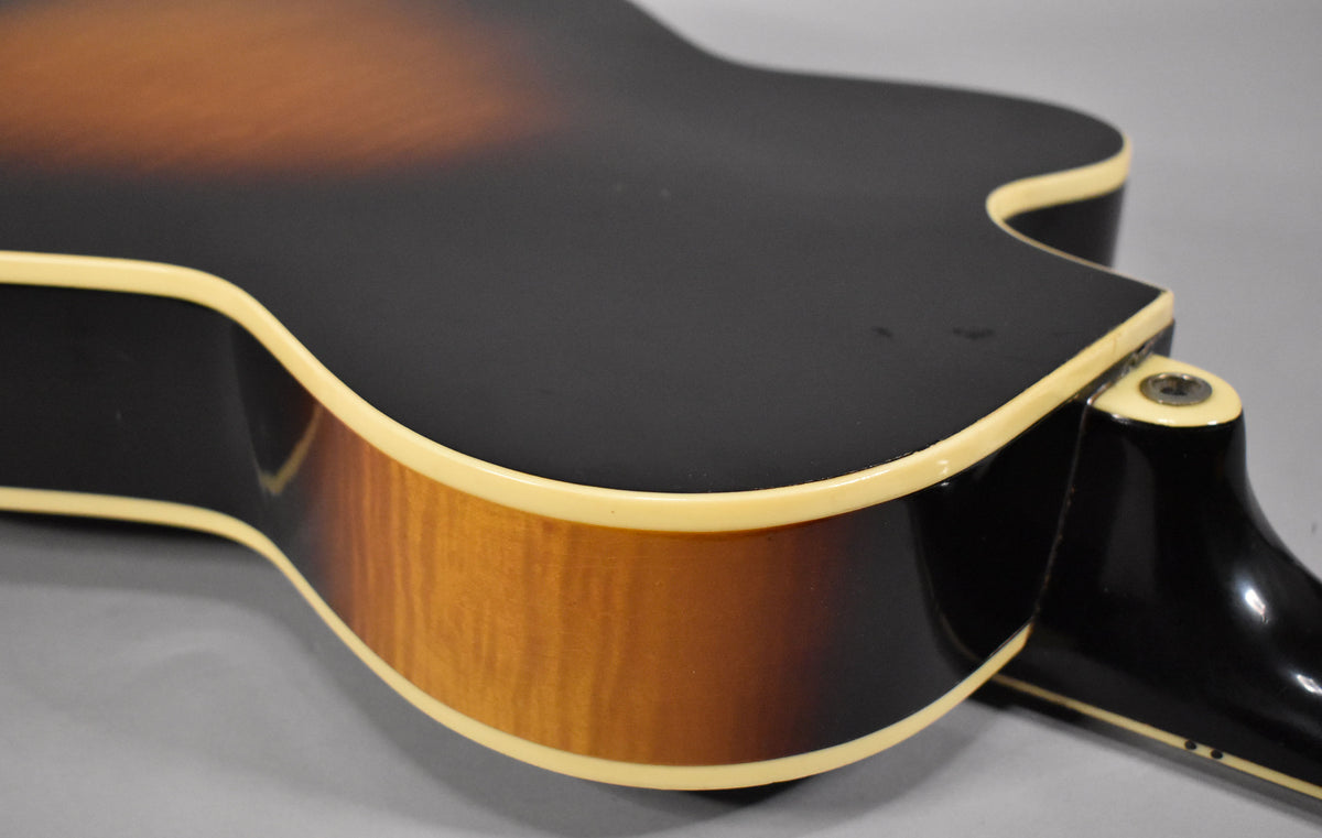 Close-up of the guitar's lower bout and cutaway, showing the dark sunburst top, flame maple sides, and cream binding with some wear.