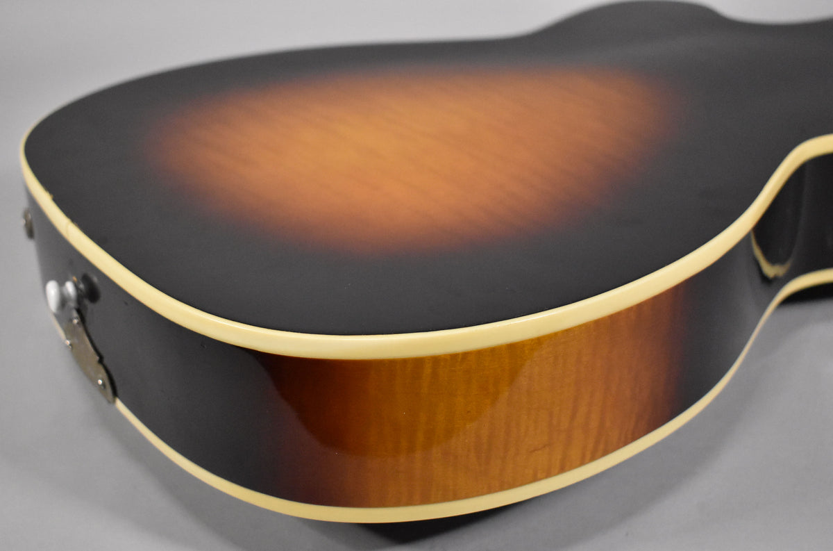 The lower bout of a sunburst archtop guitar, showing the dark brown top fading to amber, with cream binding and a strap button.