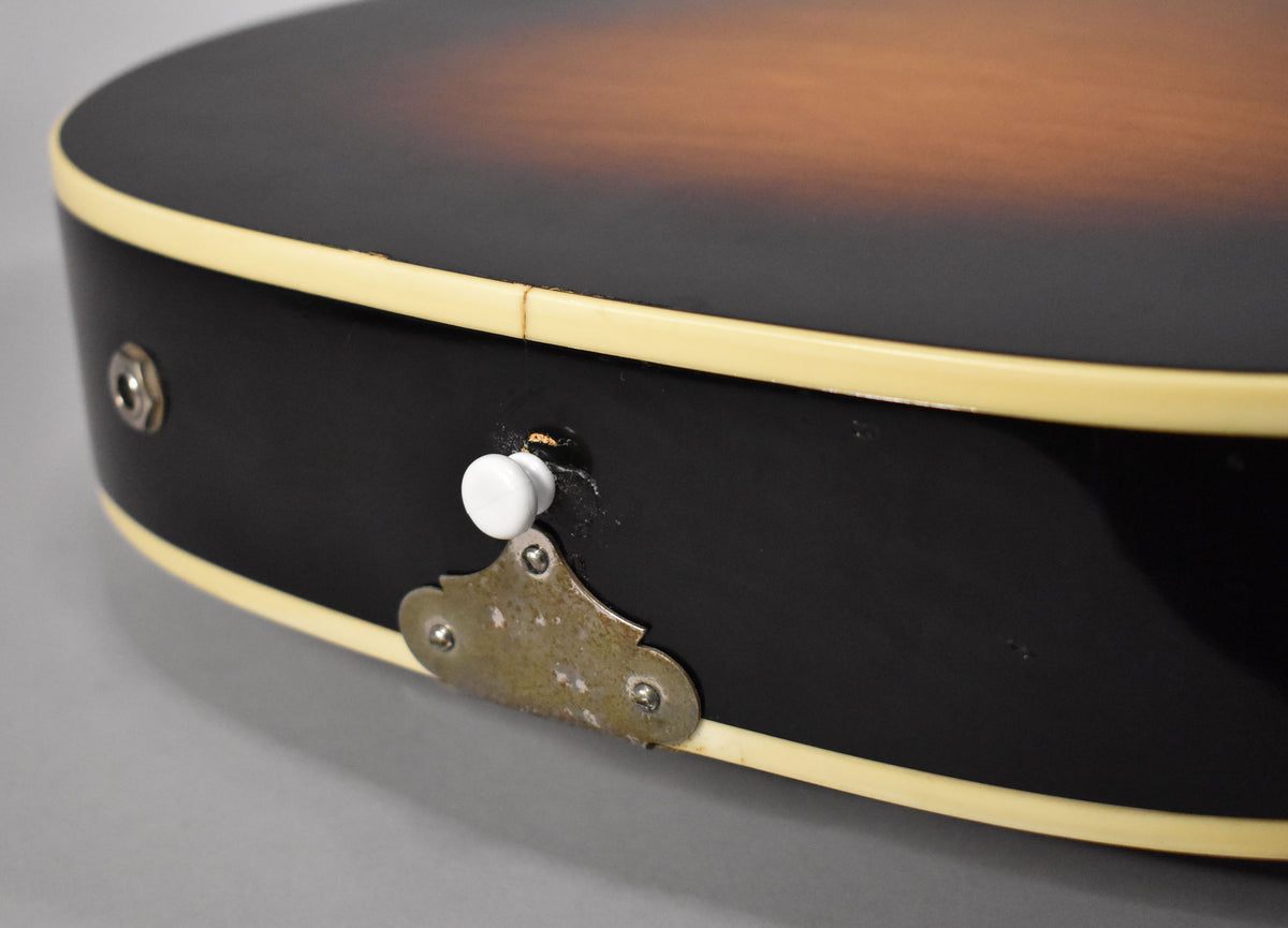 Close-up of the guitar's lower bout, showing the sunburst top, black sides with cream binding, output jack, and a worn strap button.