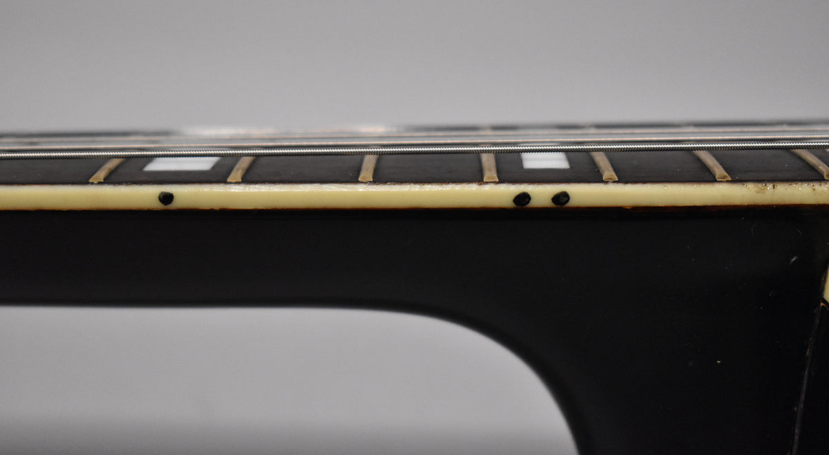 Close-up of the guitar's dark fretboard, showing white block inlays, side dots, and cream binding with visible wear.