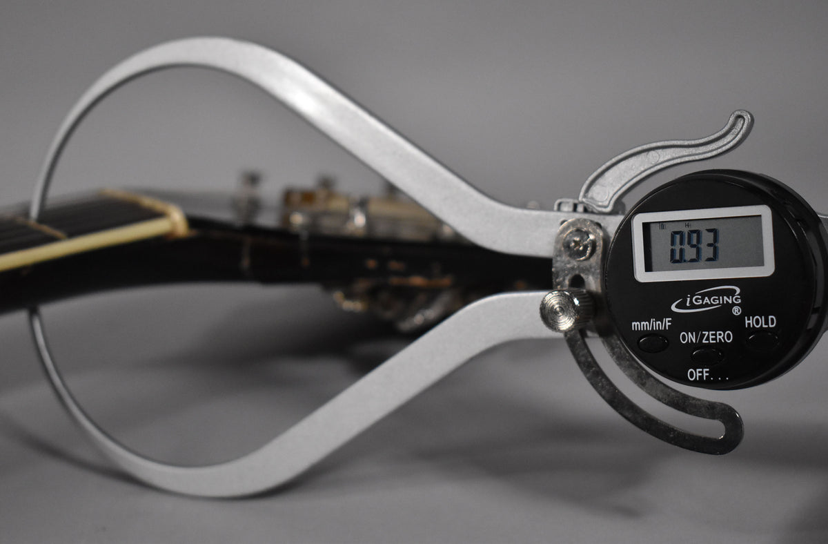 A digital caliper measures the guitar's nut width at 0.93 inches, with the sunburst headstock and tuning pegs blurred in the background.