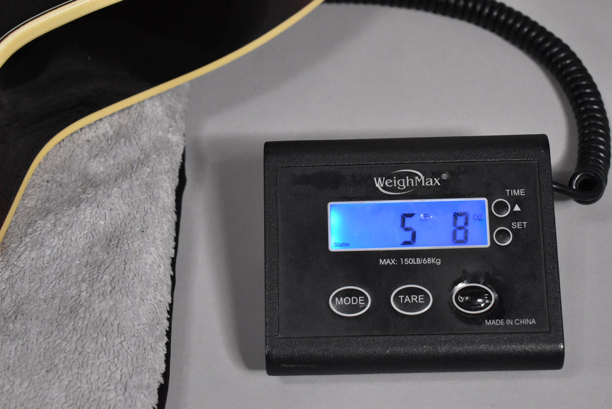 The guitar's lower bout, resting on a grey cloth, is partially visible next to a digital scale displaying "5 lbs 8 oz".