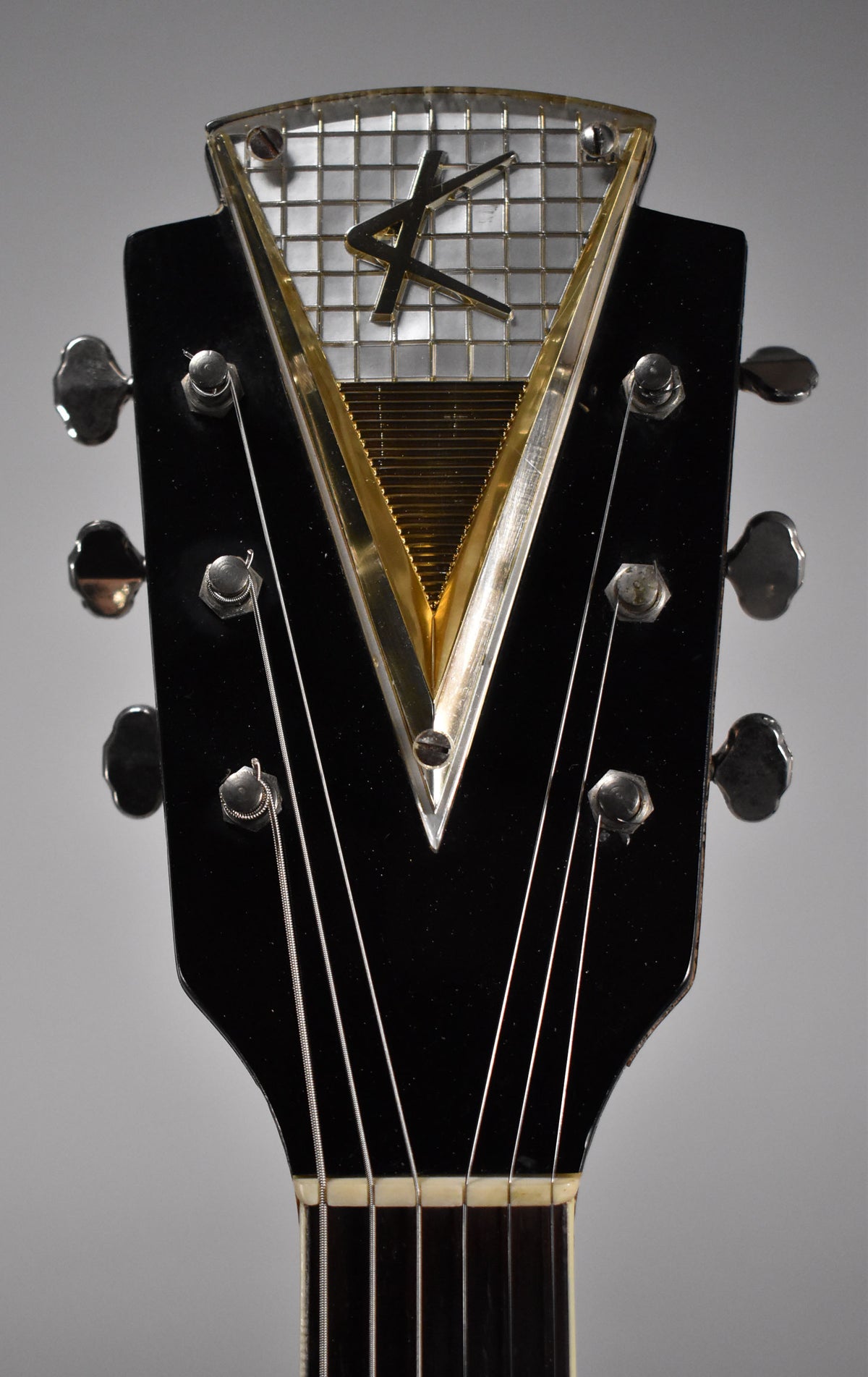 Close-up of the black headstock with six chrome tuners and a large, ornate triangular gold and silver emblem with a stylized "K".