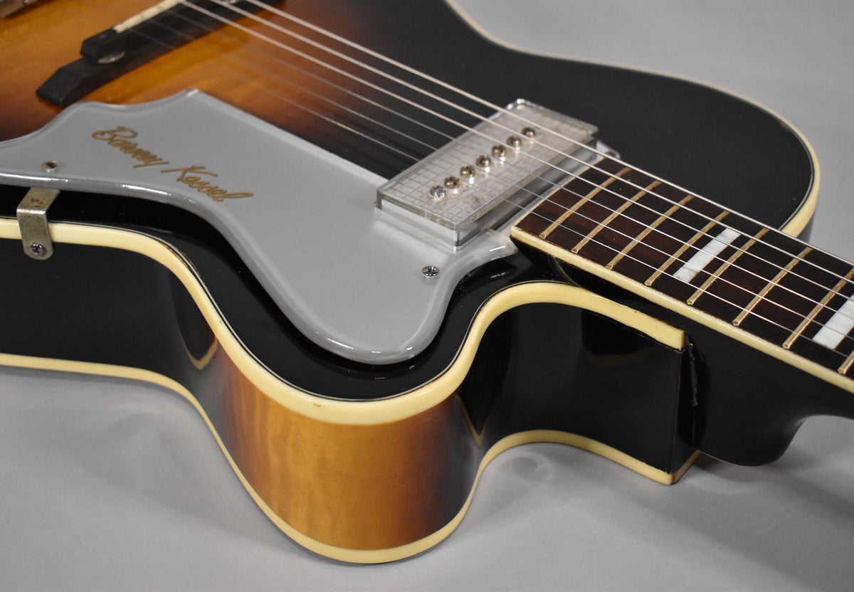 Close-up of the guitar's sunburst body and neck joint, showing the clear pickup, gray pickguard with gold lettering, and block inlays.