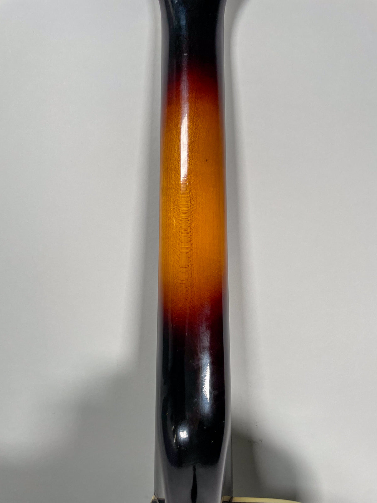 The guitar's neck, viewed from the back, shows a sunburst finish with dark brown edges fading to a bright orange-yellow center.