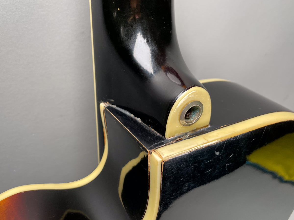 Close-up of the guitar's black neck heel and body binding, showing wear, checking, and a rusty strap button.