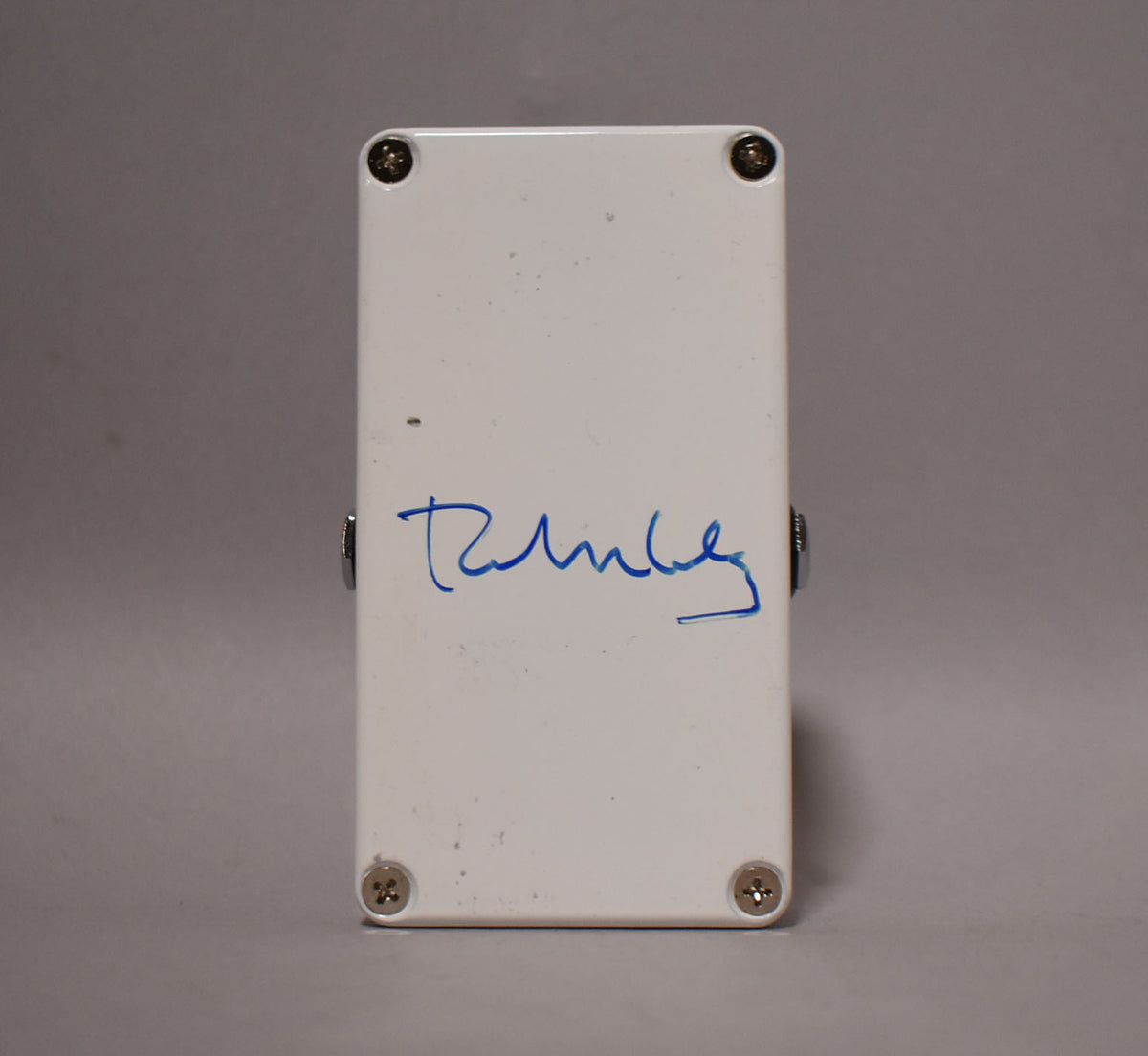 The white pedal's back panel is visible, signed in blue ink, with four silver screws and minor surface scuffs.