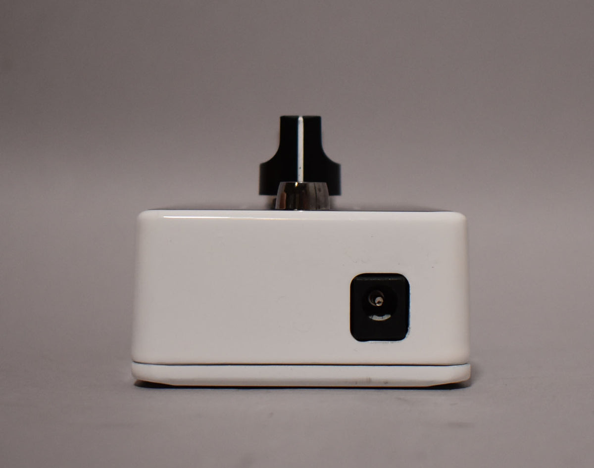 The white pedal is viewed from the front, showing a black power input jack on the right and a black control knob on top.
