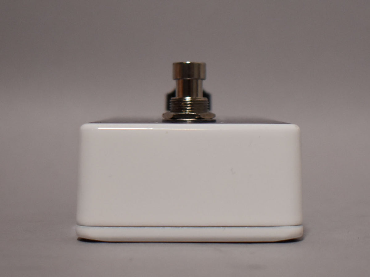 The white pedal is viewed from the front, showing a single chrome footswitch with a threaded nut, and a slight scuff on the top right edge.