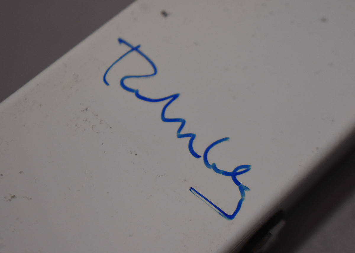 Close-up of the pedal's white casing, showing a blue signature and light scuffs, with a dark edge visible at the bottom right.