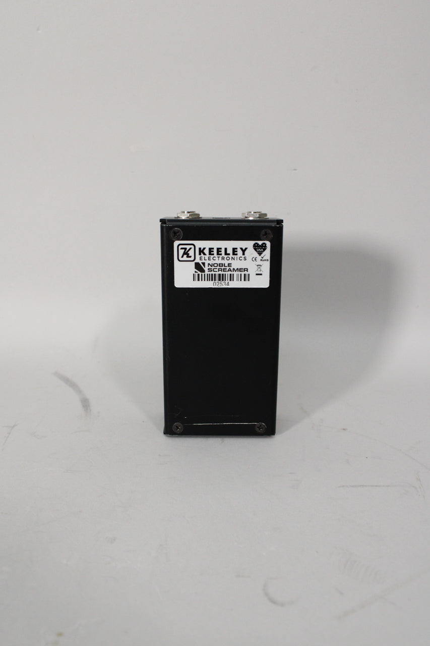 The black pedal is viewed from the back, showing a white label with a barcode and two silver input jacks on top.