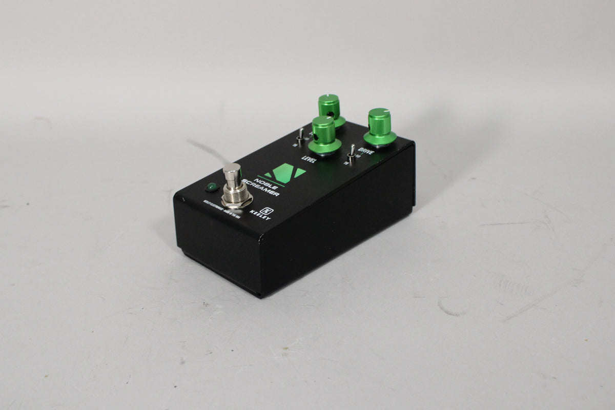 A black pedal with a green logo, three green knobs, a silver footswitch, and two small toggle switches, viewed from the front-right.