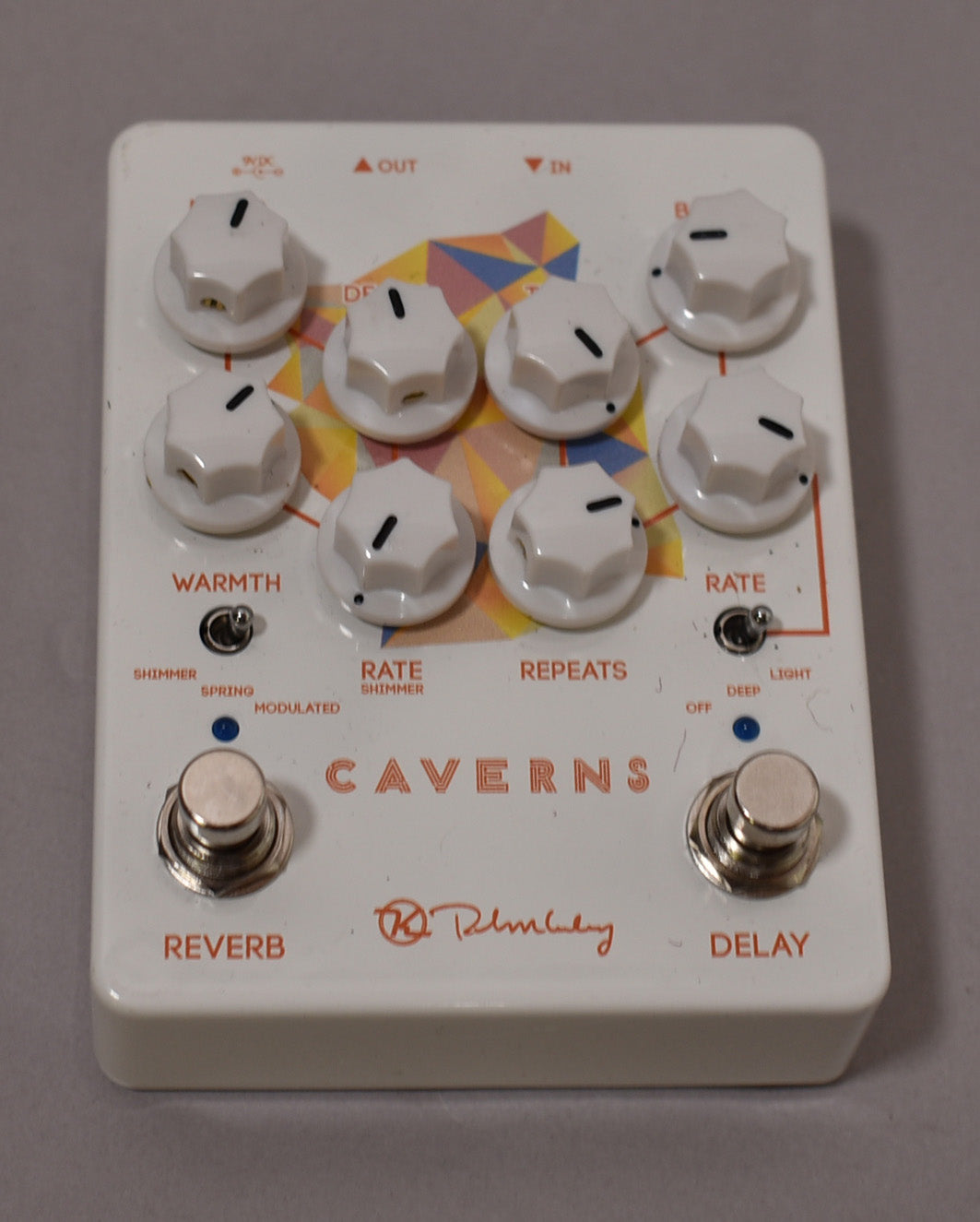 White guitar pedal with eight white knobs, two chrome footswitches, and a colorful geometric pattern on the face.